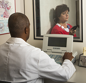 Audiologist giving hearing test to woman in sound booth.