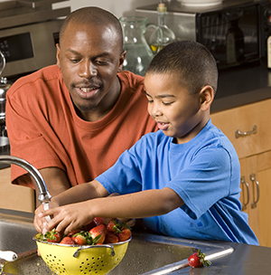 Man and boy washing strawberries in sink.