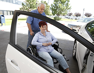 Man helping woman in wheelchair into car.