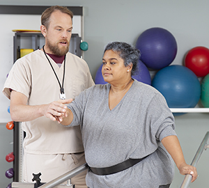 Physical therapist working with woman using parallel bars.