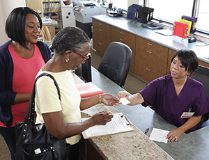 Two women talking to medical office receptionist.