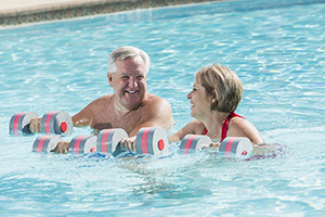 One woman and one man doing water aerobics with weights in pool.