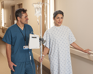 Woman patient walking in hospital hall with an IV pole and nurse.